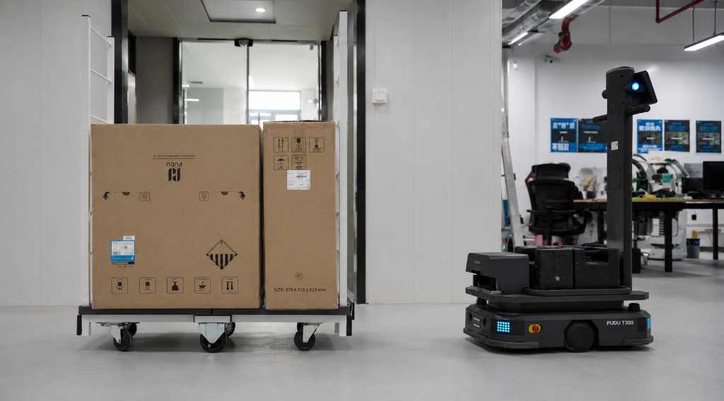 PUDU T300 com baterias substituíveis e luzes indicadoras ao lado de carrinho de carga
